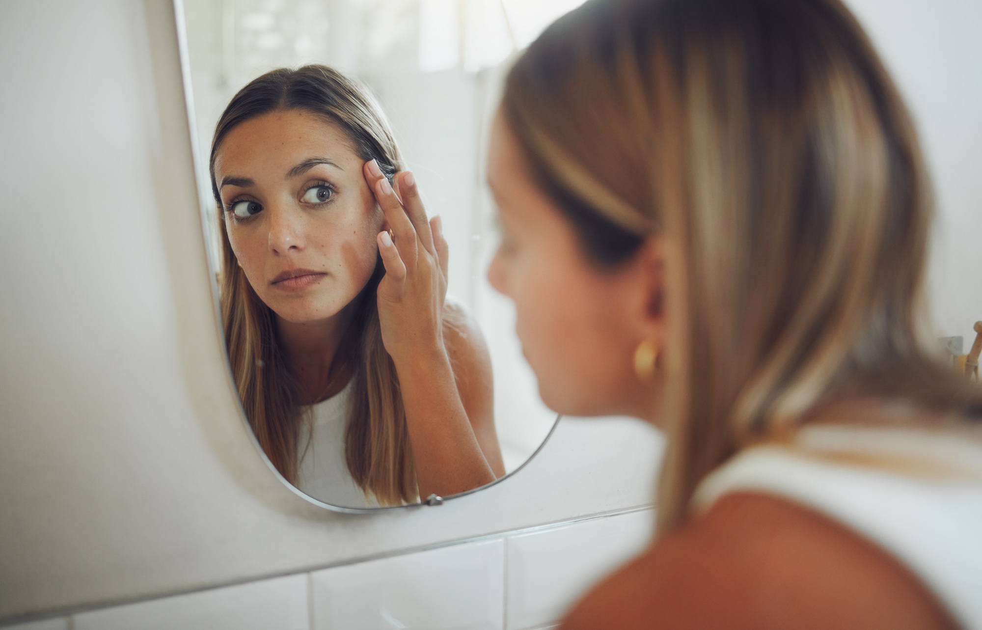 Close up of beautiful young caucasian woman looking in the mirror while touching her face and check